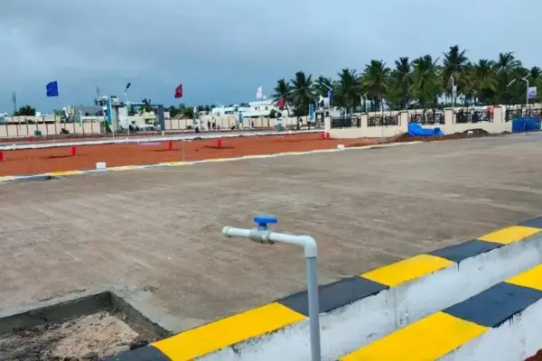 Signature City Phase 3 residential plot layout in Sulur, Coimbatore, showing paved internal roads with black and yellow kerb stones, water supply pipeline, compound wall, and coconut palm trees in the background